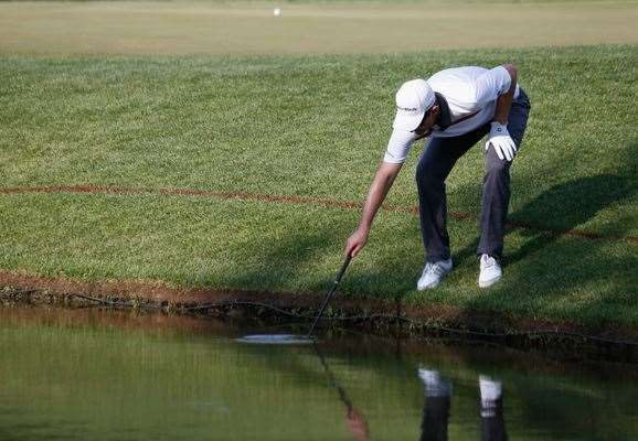 Justin Rose fishes his ball out of the water on the 18th hole during the final round. PHOTO: Getty Images