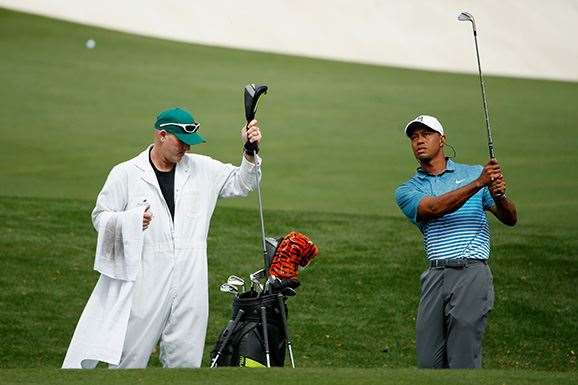 Tiger Woods hits a chip shot on the practice range as caddie Joe LaCava looks on. PHOTO: Getty Images