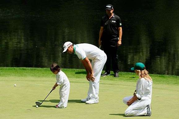Jason Day waits on a green with his son Dash as Erik Compton looks on during the Par 3 Contest. PHOTO: Getty Images.