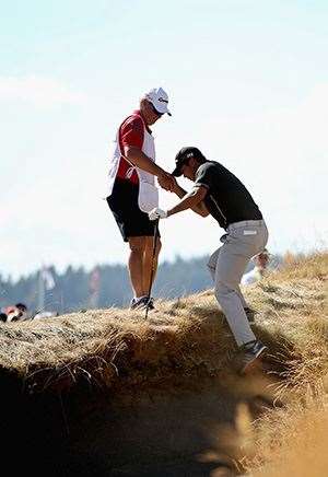 Jason Day climbs out of a bunker on the 10th hole with help from caddie Colin Swatton. (Photo by Ezra Shaw/Getty Images)