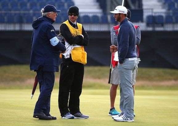 Dustin Johnson talks with a rules official on the 15th green as play is suspended due to high winds during the second round. Photo by Matthew Lewis/Getty Images.