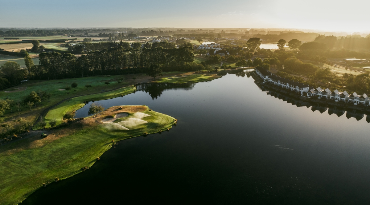 The 8th green at Clearwater Golf Club Christchurch being sprinkled with irrigation water in the evening light with the spring-fed lake visible beyond and the Southern Alps in the background