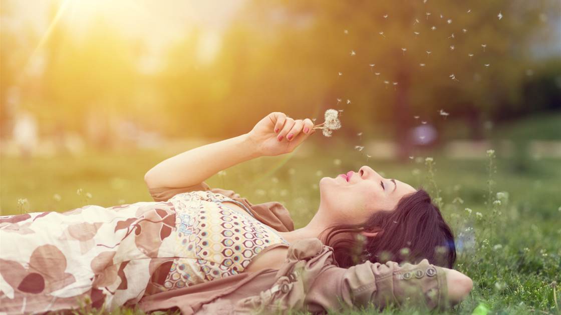 A woman relaxing in the grass while blowing on a dandelion clock A woman relaxing in the grass while blowing on a dandelion clock