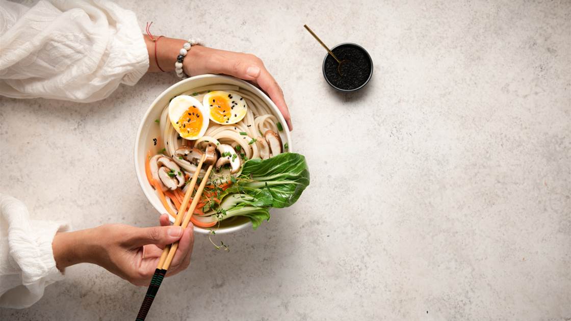 Hands holding a noodle bowl full of Asian foods that have health benefits like bok choy Hands holding a noodle bowl full of Asian foods that have health benefits like bok choy