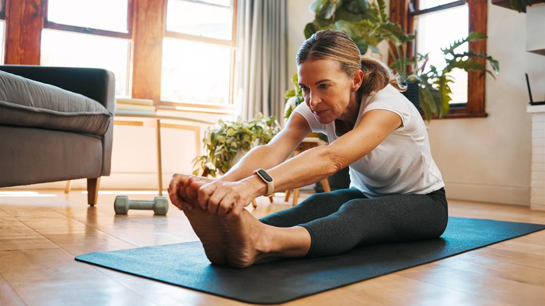 Middle-aged woman stretching glutes on yoga mat at home Middle-aged woman stretching glutes on yoga mat at home
