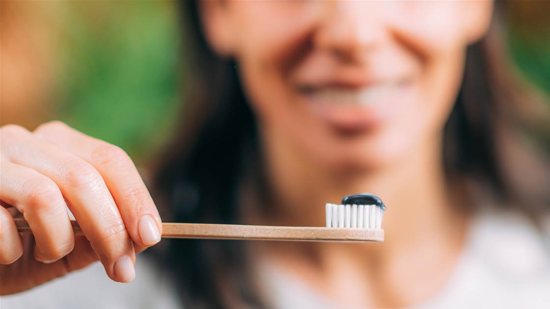 Woman holding a toothbrush with black charcoal toothpaste — does it whiten or damage enamel? Woman holding a toothbrush with black charcoal toothpaste — does it whiten or damage enamel?